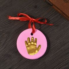 a pink ornament with a hand print on it and a red ribbon around the edge