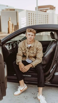 a young man sitting in the open door of a car