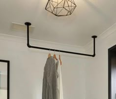 clothes hanging on rail in white room with mirror and light fixture over door way,