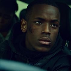 a close up of a person sitting in a car wearing a hoodie and looking at the camera