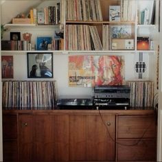 an old record player is sitting on top of a wooden cabinet in front of a wall full of records