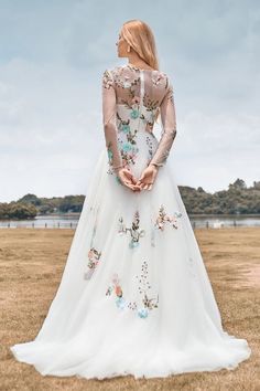 a woman in a white wedding dress standing on the grass with her back to the camera