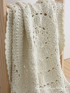 a white crocheted blanket hanging on a wooden rail with wood slats in the background