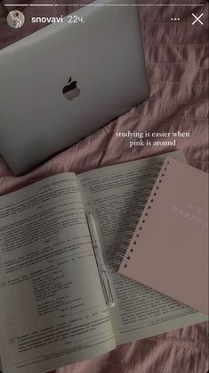 an open book sitting next to a laptop computer on top of a pink sheet covered bed