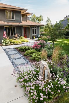 a house with flowers in the front yard and an american flag on the side walk