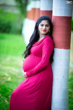 a pregnant woman leaning against a tree in a pink dress