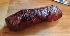 a piece of meat sitting on top of a wooden cutting board next to a knife