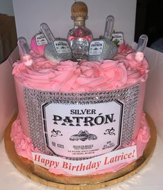 a birthday cake with pink frosting and bottles on top, sitting in a box