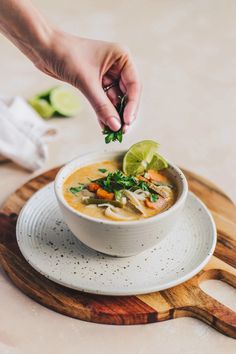 a person is dipping some lime into a bowl of soup on a wooden board with a cutting board