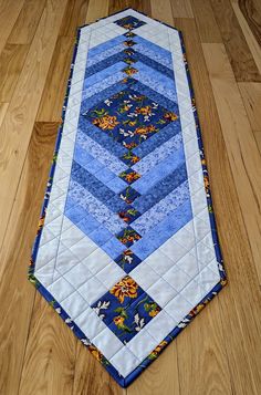 a blue and white quilted table runner on the floor with wood floors in the background