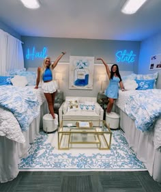 two women in blue dresses standing next to each other on twin beds with lights above them