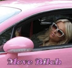 a woman sitting in a pink car with her head out the window and wearing sunglasses