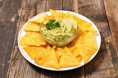 a white plate topped with chips and guacamole on top of a wooden table