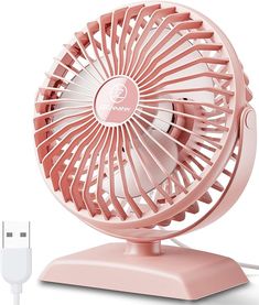 a pink fan sitting on top of a table next to a charger and plugged in