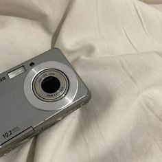 a silver digital camera sitting on top of a white bed sheet with the cover pulled down