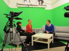 three people sitting on a couch in front of a green screen with camera equipment around them