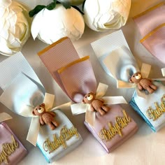 there are five small pink and blue gift bags with teddy bears on them next to white flowers