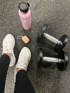 a person standing next to two dumbbells and a pink water bottle on the ground