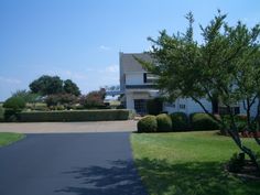 a driveway leading to a large house with trees in the foreground and bushes on either side