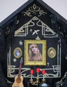 a guitar sitting next to a painting on a black cloth with gold trimmings