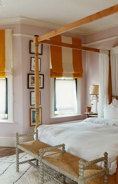 a bedroom with pink walls, white bedding and pictures on the wall above it