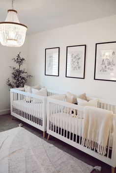 a white crib in a room with two pictures on the wall and a chandelier