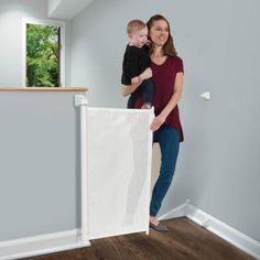 a woman holding a baby in her arms while standing next to a white curtain on the wall