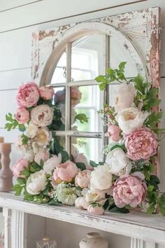 a white fireplace mantle with pink flowers and greenery on it, next to a mirror