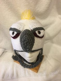 a crocheted bird wearing a scarf and hat on top of a white sheet