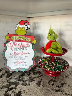 the grinch is sitting on top of the table next to the christmas dinner sign