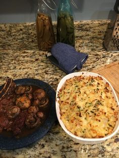 a table topped with two plates of food next to a bowl of meat and potatoes