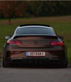 the rear end of a brown car parked in front of a grassy area with trees