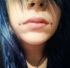 a woman with blue hair has piercings on her nose