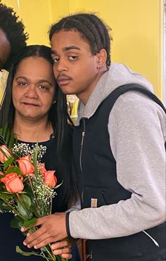 two people standing next to each other with flowers in front of them and one person holding a bouquet