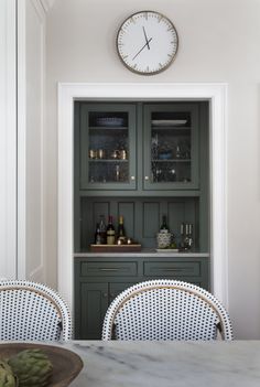 a dining room table with chairs and a clock on the wall above it's cabinets