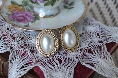 Vintage large oval clip-on earrings showcase a large faux ivory pearl set in an ornate gold tone classic detailed setting, giving these classy rich look!  Clip-in earrings are in good vintage condition showing minimal wear for their age, such as a little scuffing to the faux pearl centers. Please see all photos as this is part of description. Measurements: Height: 1 1/4" Width: 1" Weight of each earring: .2 oz. Pearl Look, Costume Earrings, Ivory Pearl, Pearl Set, Clip Ins, Costumes For Women, Costume Jewelry, Faux Pearl, Clip On Earrings