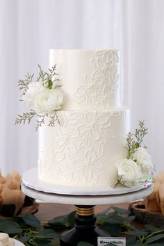 a white wedding cake with fresh flowers on the top and side, sitting on a table