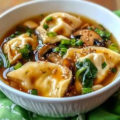 a white bowl filled with dumplings covered in broth and green vegetables on top of a green napkin