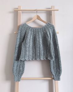 a knitted sweater hanging on a wooden hanger next to a white wall and clothes rack