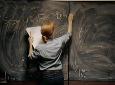 a woman writing on a blackboard in front of two chalkboards with writing on them