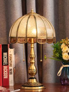 a lamp sitting on top of a wooden table next to a vase filled with flowers