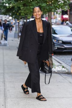 a woman is walking down the street in her black suit and sandals, smiling for the camera