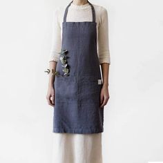 a woman standing in front of a white wall wearing an apron with flowers on it