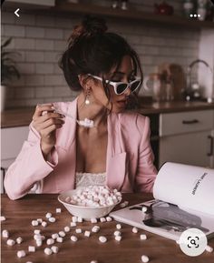 a woman sitting at a table eating marshmallows from a bowl and reading a book