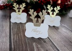 three place cards with gold glitter reindeer antlers on them, sitting on a wooden table