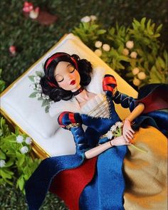 a close up of a doll laying on a pillow with flowers in the grass behind it