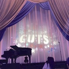 people are sitting in front of a stage with a piano and stars on the curtain