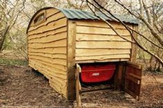 an outhouse in the woods with its door open and a red bucket inside it