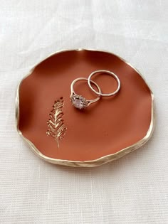 two wedding rings sitting on top of an orange platter with a small flower in the middle