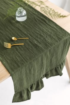 a green table cloth with gold utensils on it and a vase filled with greenery